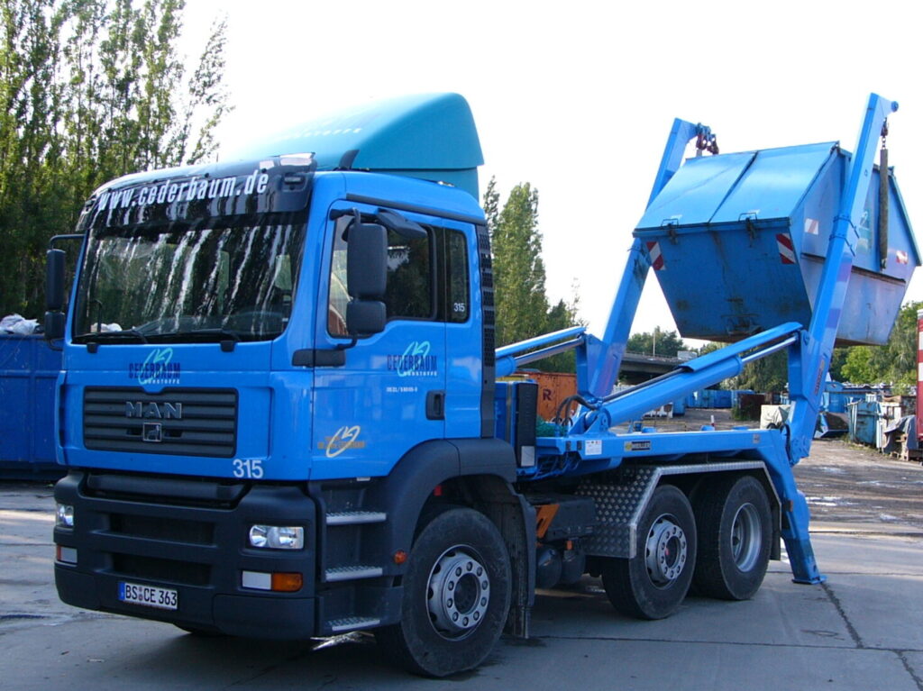 ein blauer Absetz-LKW der grade einen blauen Container absetzt